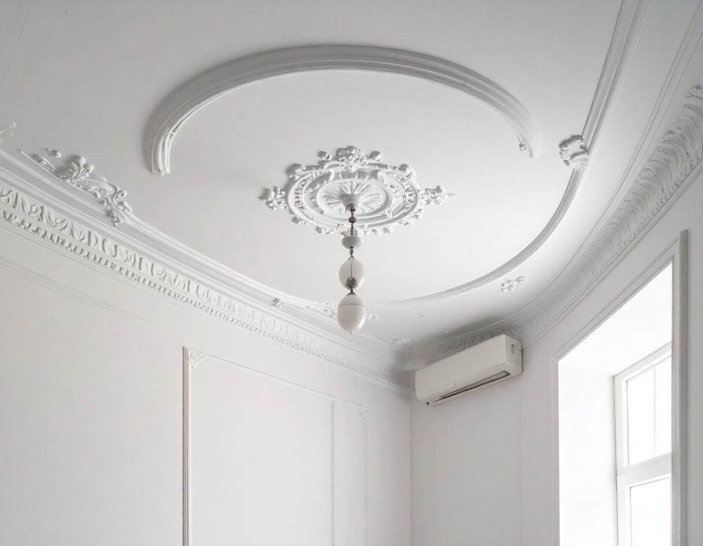 weißer kreisförmiger Deckenstuck mit einer langen goldenen Lampe in der Mitte als Veranschaulichung von Stuckarbeiten vom Stuckateurbetrieb in Kleve